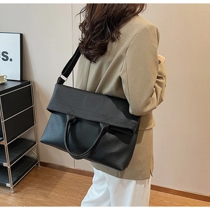 Detail einer schwarzen Tote-Bag aus genarbtem Leder mit Klappe und Tragegurt