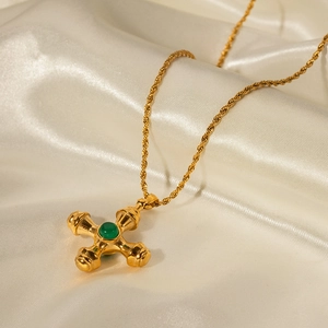 Close-up of 18k gold stainless steel cross pendant with green gem on white silk
