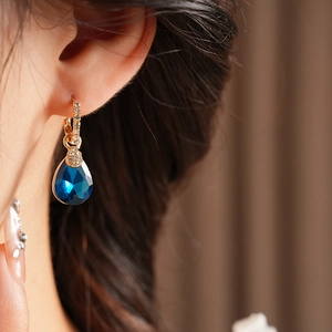 Gros plan sur une créole dorée ornée d'une pierre goutte bleue et pavé de diamants