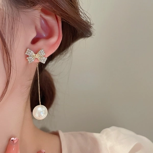 Dettaglio di eleganti orecchini a fiocco con strass brillanti e perle bianche cadenti