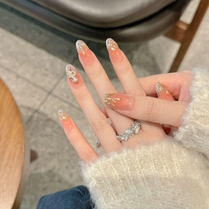 Detail of peach gradient press-on nails with 3D floral charm and gold leaf accents