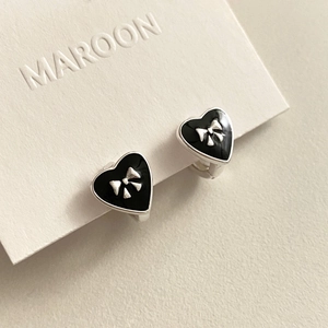 Detail of silver heart hoop earrings with black enamel and 3D bow accent on a display board