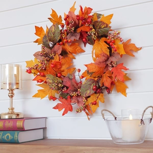 Autumn wreath with maple leaves and berries on white wooden wall with candles