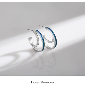 Close-up of silver earrings featuring blue enamel and micro-pave clear gemstones detail