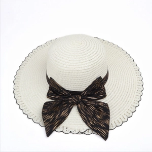Close-up of beige woven sun hat featuring a wide black ribbon with metallic gold stripes