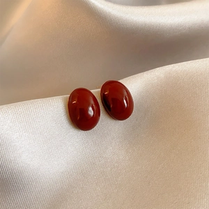 Elegant red oval resin stud earrings resting on luxurious white silk fabric