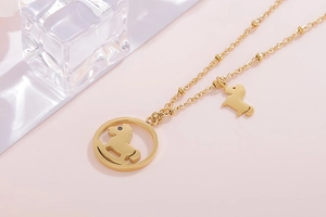 Détail d'un collier en acier doré avec pendentif cheval à bascule sur fond rose