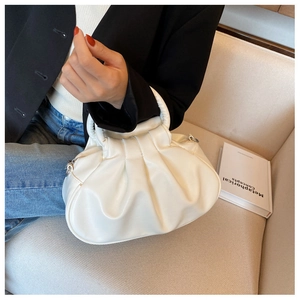 Detail of a pleated cloud handbag in cream white PU leather held by a model in a black suit
