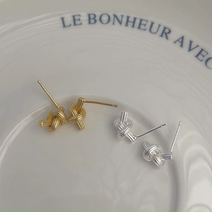 Detail of gold and silver knot earrings with spiral texture on a white plate