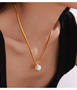 Detail of a minimalist gold snake chain necklace with a round white pearl pendant