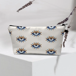 Close-up of cream evil eye makeup bag with black zipper on a white geometric platform