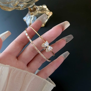 Detail view of gold bow bangle and cubic zirconia double-layer bracelet on wrist