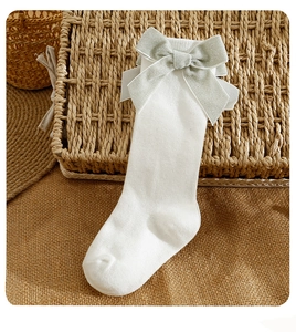 Close-up of white knee-high socks with a large grey-green bow and fine knit texture
