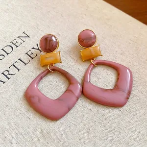 Geometric resin drop earrings with pink marble and mustard yellow patterns on beige fabric
