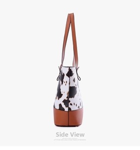 Side view of large cow print tote bag with brown leather base and shoulder strap details