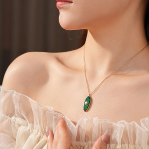 Detail of vintage gold necklace with green oval pendant and pearl worn by a model