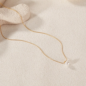 Macro detail of a minimalist gold pearl necklace on a premium stone textured surface