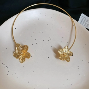 Detailed close-up of golden metal flower choker with 3D embossed petals on a ceramic tray
