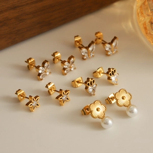 Golden butterfly and star stud earrings set with zircon and pearls on warm background