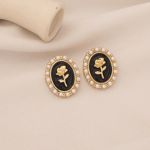 Vintage gold rose earrings with black enamel and white pearls on elegant white fabric