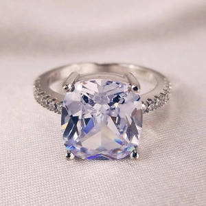 Macro shot of square-cut silver engagement ring with small side crystals on soft fabric