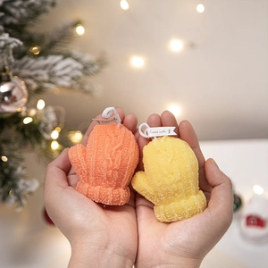Orange and yellow glove-shaped scented candles held in hands for Christmas decoration