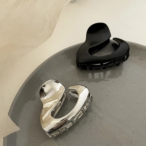 Macro detail of heart-shaped metal hair claws in matte black and silver on ceramic tray