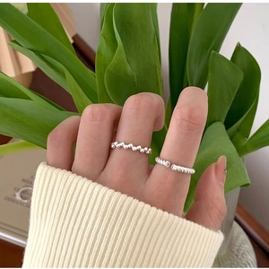 Detail of twisted rope and beaded stackable silver rings worn with a floral backdrop