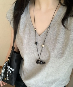 Detailed close-up of a vintage wood gourd pendant necklace on a grey sweater