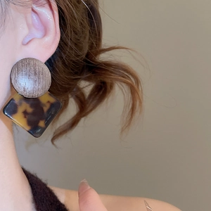 Macro detail of tortoiseshell resin diamond pendant and brushed metal round earring stud