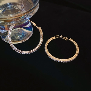 Dettaglio di orecchini a cerchio dorati con strass scintillanti su sfondo elegante