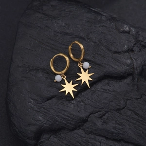 Détail de créoles plaquées or 14K avec breloques étoiles et perles sur pierre noire
