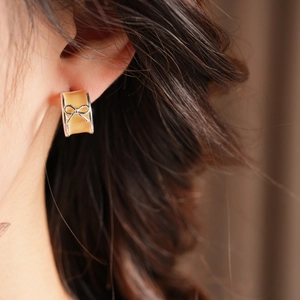Detail of C-shaped bow earring featuring yellow enamel and silver-tone ribbon detail