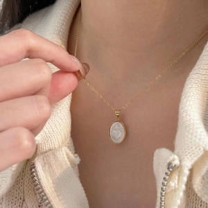 Close-up of golden oval shell pendant with heart relief on a minimalist necklace