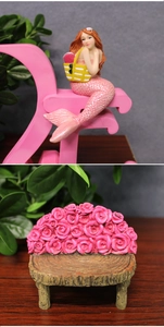 Detail view of resin mermaid figurine with flower basket and a pink rose garden bench seat