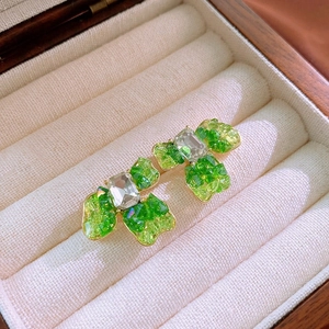 Detailed close-up of green crystal-encrusted bow earrings with a golden metallic base