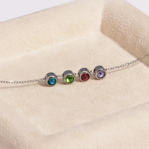Gros plan d'un collier en argent avec quatre zircons colorés sertis en clos circulaires