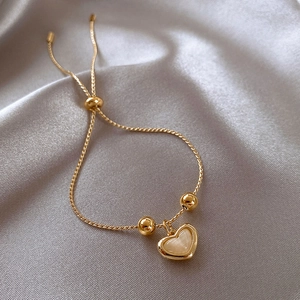 Detailed shot of an adjustable gold heart bracelet on a soft grey silk fabric