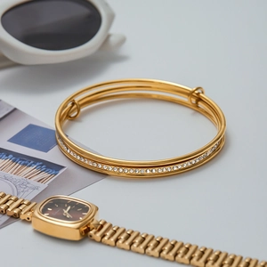 Detail of a triple-layered gold zircon bracelet next to white sunglasses on grey surface
