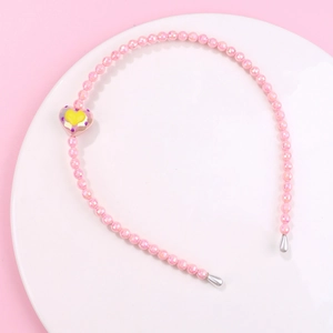 Detailed view of pink beaded headband for girls with rainbow heart charm on white tray