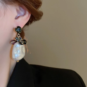 Close-up of baroque pearl earrings with sparkling beads and dark gemstone on a model