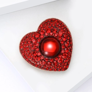 Close-up of heart-shaped brooch with red rhinestones and a central red pearl detail