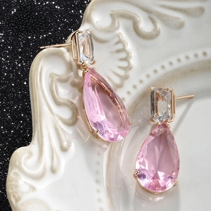Detailed view of pink pear-cut crystal earrings with gold claw settings on white ceramic