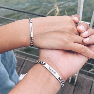 Macro shot of silver Cuban chain bracelets with engraved name tags for couples