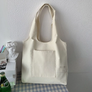 Detail of cream canvas tote bag with front pocket on a blue checkered tablecloth