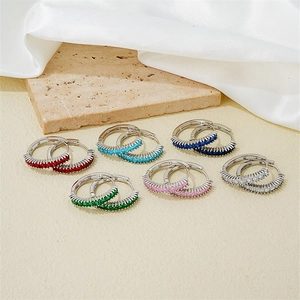 Set of six silver hoop earrings with multicolored cubic zirconia on a stone surface
