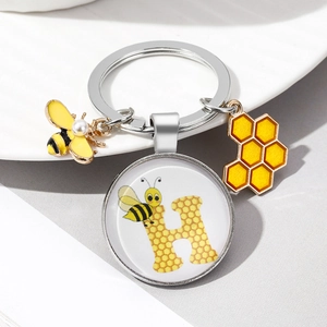 Close-up of silver bee keychain with honeycomb pendant and glass dome letter H charm