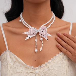 Detail of faux pearl sweater chain featuring pink polka dot ribbon bow and pendant