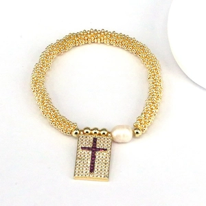 Detail view of golden beaded bracelet with zircon cross rectangle charm and white pearl