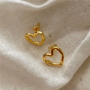 Detail of gold hollow heart earrings with irregular texture on white woven fabric